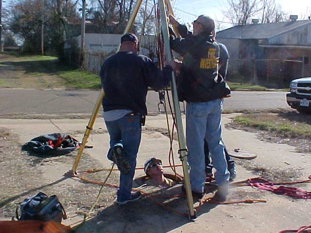 Fire fighters examine the rigging, while one waits in the manhole.